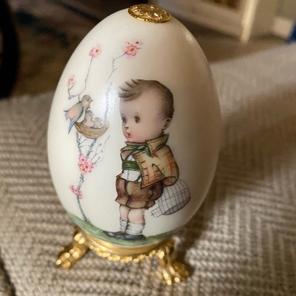 Egg on golden stand w/a boy and a bird and some flowers